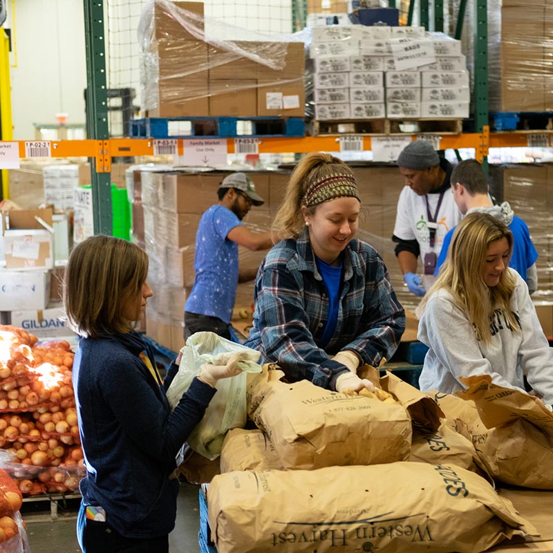 Three women in a warehouse organizing large sacks of food.