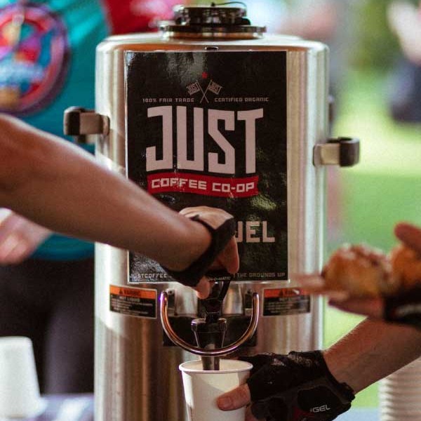 A photo of a large coffee drip machine and people's arms serving coffee into paper cups.