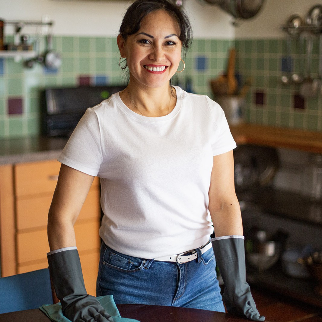 A half/body image of a woman smiling, in a white t-shirt and cleaning gloves